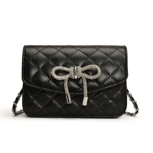 Detailopname van een zwarte gewatteerde crossbodytas met een fonkelende strass strik.