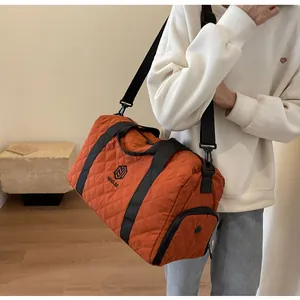 Detailed view of the orange quilted travel duffel bag carried by a fashion model.