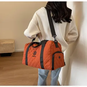 Large orange quilted travel duffel bag carried on shoulder by woman in casual wear