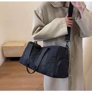 Black quilted duffel bag for travel and gym shown on model in a stylish trench coat