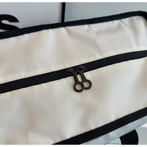 Dettaglio delle doppie cerniere nere con tiranti circolari su borsa da viaggio in tela bianca.