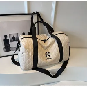 Quilted diamond lattice travel bag with black handles in minimalist studio setting.