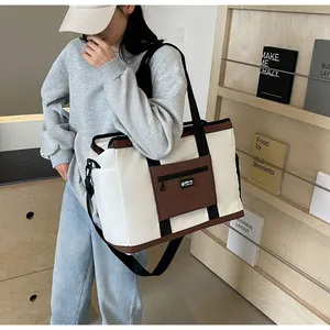 Borsa da viaggio in tela capiente con dettagli marroni mostrata a spalla dal modello.