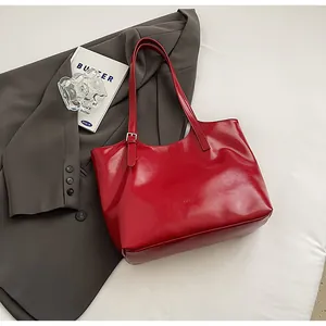 Close-up view of a bright red glossy leather tote bag set on a grey blazer garment