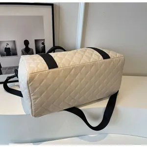 Side view of cream quilted travel duffel bag showing black nylon straps and texture