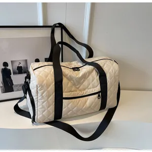 Detail view of cream quilted duffel bag with black straps for travel and fitness.