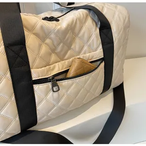 Detail view of cream quilted duffel bag featuring a functional front zipper pocket