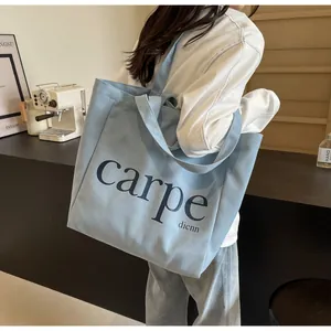 Detailed view of a stylish light blue canvas tote bag with carpe print carried over the shoulder