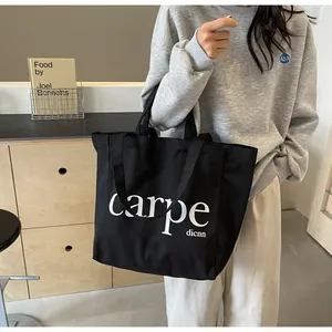 Model carrying a large black canvas tote bag with carpe letter print in a modern setting