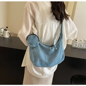 Back view of a stylish large blue denim crescent bag worn by a model in a cafe setting