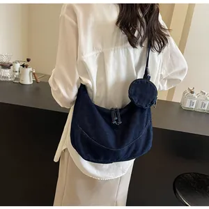 Detailed view of a stylish navy blue denim hobo bag worn crossbody in a cafe setting.