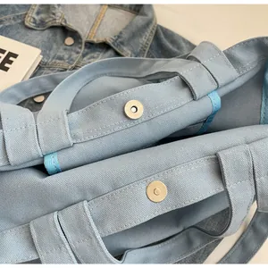 Detail of magnetic snap closure on light blue canvas tote bag with woven straps