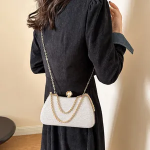 Detailed view of an elegant white textured evening clutch bag featuring a gold chain strap