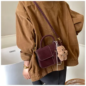 Detailed view of burgundy suede saddle bag featuring cute teddy bear charm on model