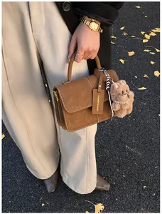 Close-up of a stylish brown saddle handbag held by a woman on a ginkgo leaf path