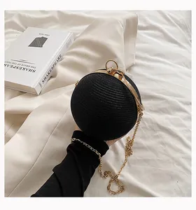 Detail view of a stylish round black evening clutch with a textured finish and gold chain.