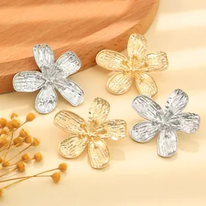 Close-up detail of vintage textured five-petal flower earrings in gold and silver finish