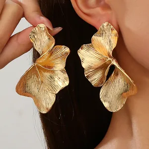 Macro detail of oversized gold textured leaf-shaped double-layer flower earrings