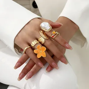 Detailaufnahme von Barockperlen- und orangefarbenen Blumenringen an der Hand in Weiß