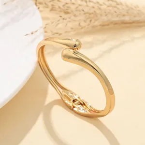 Dettaglio ravvicinato di un bracciale rigido dorato minimalista con motivo a onde irregolari