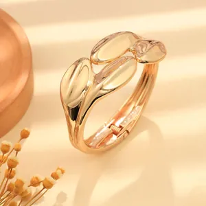 Dettaglio di un bracciale rigido dorato minimalista con onde irregolari e lucide.