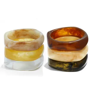 Close-up of polished wide resin bangles featuring irregular marble and amber patterns