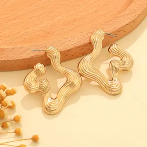 Detailed view of gold wavy earrings with vintage striped texture on wooden tray.