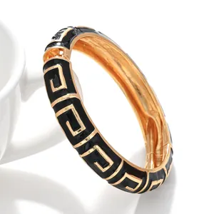 Detailansicht eines goldenen Armreifs mit schwarzen geometrischen Emaille-Mustern.