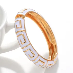 Detailaufnahme eines weißen Emaille-Armreifs mit goldenem griechischem Muster.