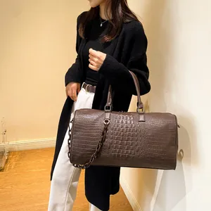 Detailed macro view of a stylish brown crocodile pattern travel bag held by a model