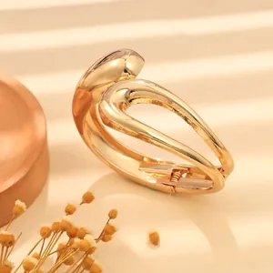 Dettaglio ravvicinato di un bracciale rigido dorato minimalista con motivo a onde irregolari