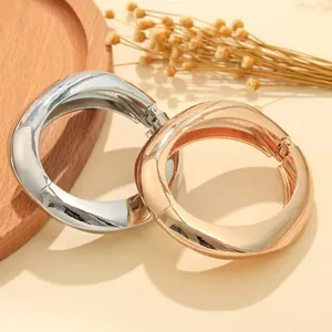 Dettaglio di bracciali minimalisti a onde irregolari in argento e oro lucido.