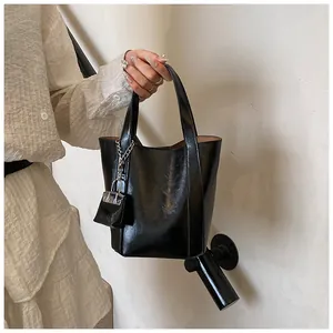 Detailaufnahme einer glänzenden schwarzen Beuteltasche mit dekorativem Anhänger.
