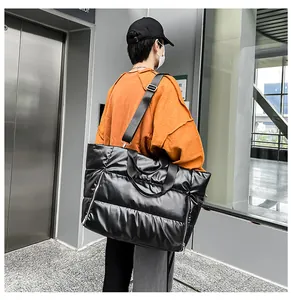 Gran bolso de viaje acolchado negro llevado por un modelo en una terminal moderna.