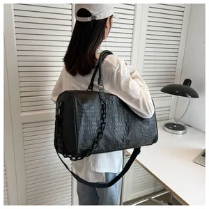 Black faux-crocodile leather weekender bag carried by a model in a modern room