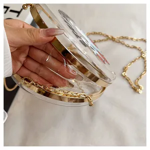Macro detail view of a round transparent acrylic crossbody bag with elegant gold chain strap.
