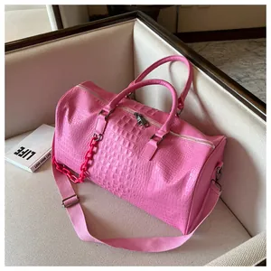 Close-up detail of large pink crocodile pattern leather travel bag on a beige couch