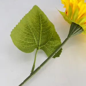 Nahaufnahme einer leuchtend gelben künstlichen Sonnenblume mit grünen Blättern.