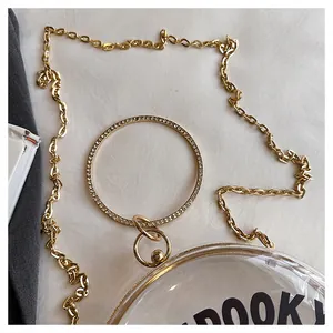 Close-up of transparent round bag with gold chain and crystal handle details.