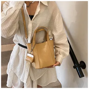 Minimalistische khakifarbene Eimertasche mit passendem Mini-Anhänger am Modelhand