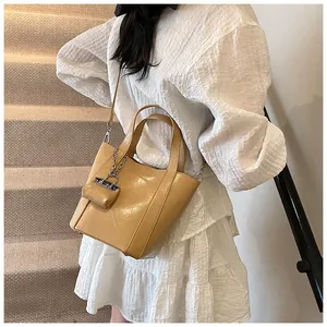 Detailansicht einer khakifarbene Eimertasche mit Mini-Anhänger, getragen von einem Model