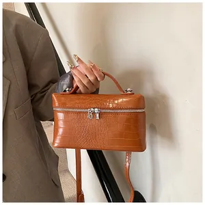 Detailed view of a brown crocodile pattern box bag held by hand with shoulder strap
