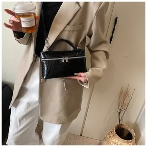 Close-up lifestyle view of a chic black crocodile pattern box handbag held by a model.