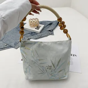 Dettaglio di borsa a mano elegante con stampa di bambù e manico in perle di legno
