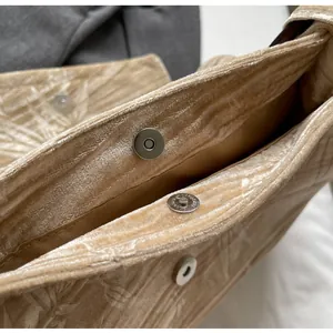 Primer plano de bolso de terciopelo beige con patrones florales y cierre magnético