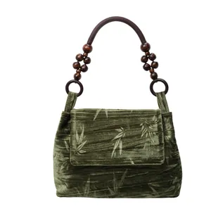 Vista detallada de bolso de terciopelo verde con estampado de bambú y asa de cuentas