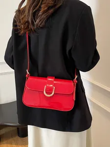 Gedetailleerd beeld van een rode lakleren crossbodytas met een gouden U-vormige gesp.