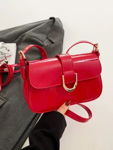 Gedetailleerde weergave van rode lakslederen crossbodytas met gouden hoefijzergesp