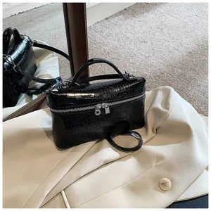 Close-up of black crocodile pattern box bag on a beige blazer accessory detail.