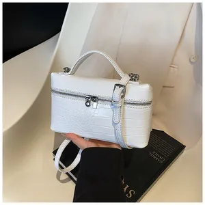 Detailed view of white crocodile pattern box bag held by hand with elegant suit background